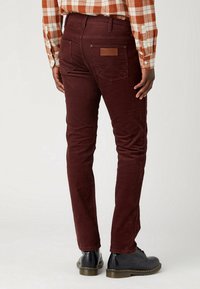 Burgundy cordoroybyxor med en figursydd design, bakfickor och en läderlogotyp. Bärs med svarta skor för kontrast.