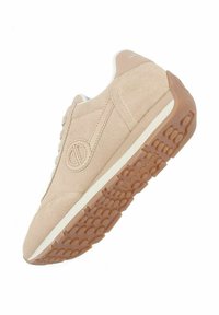Beige suede sneaker with white accents, round toe, and textured rubber sole featuring circular patterns. Side logo detail visible.