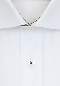 Chemise blanche à col classique, avec un bouton noir et une doublure de col à motif. Tissu lisse à la texture nette.