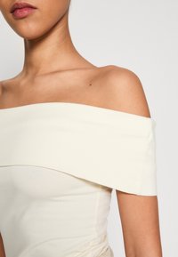 Bodysuit bez ramínek v barvě off-white, s hladkým materiálem, obepínajícím střihem a jemnou texturou. Švy po stranách.