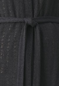 Primo piano di un tessuto nero lavorato a maglia legato in un semplice nodo che somiglia a una cintura o una fascia.