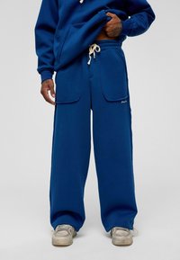 Blauwe sweatpants met grote vo pockets, een trekkoord in de taille en een ontspannen pasvorm. Gemaakt van zacht materiaal met een gladde textuur.