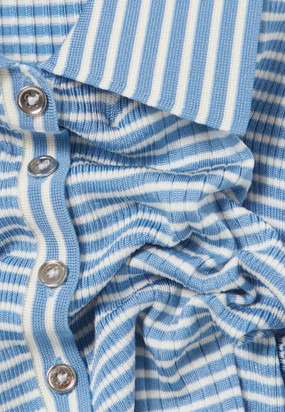 Tela a rayas azul y blanca con un punto texturizado, botones visibles y una caída relajada. Las rayas varían en ancho.