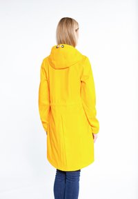 Abrigo impermeable amarillo con capucha, que cuenta con una cintura ajustada y mangas largas. Textura suave y diseño de longitud media con un dobladillo ligeramente redondeado.