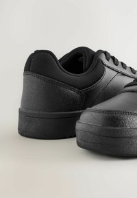 Baskets noires avec une semelle en caoutchouc texturé, un dessus en cuir lisse et des accents en tissu noir, dotées de lacets et d'un design de pointe arrondie.