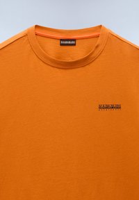 Orange bomulds-t-shirt med rund hals, der har et lille sort logo på brystet. Glat tekstur og korte ærmer.