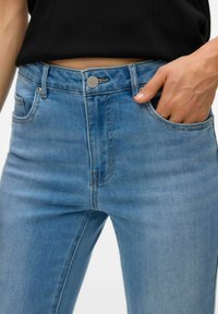 Helesinised teksapüksid kõrge vöökohaga, millel on viis taskut, metallist nupp ja peened õmblused õmbluste ääres.