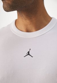 Hvid bomulds T-shirt med et sort Jumpman-logo på brystet. Udhulningen har en ribbet finish for ekstra tekstur.