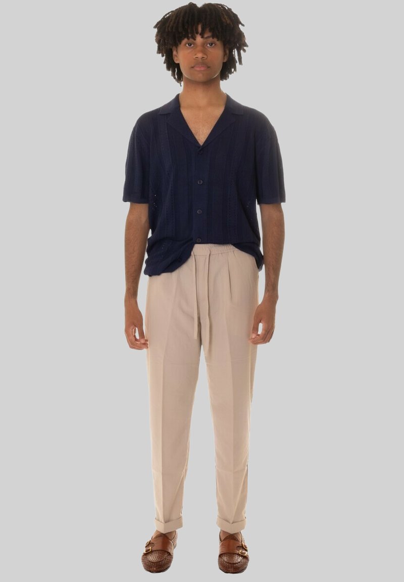 Camicia a maniche corte blu navy con bottoni e strisce verticali, abbinata a pantaloni tapered color crema e scarpe slip-on in tessuto intrecciato marroni.