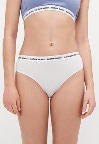 Fehér pamut bugyi alacsony szabással és fekete rugalmas derékrésszel, amelyen a "BJÖRN BORG" felirat ismétlődő mintában szerepel.