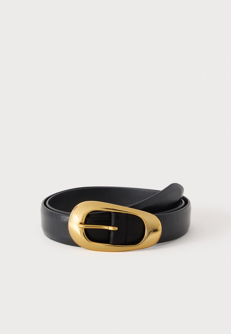 Ceinture en cuir noir roulée avec une grande boucle ovale dorée brillante sur un fond clair uni.