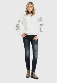 White hoodie with gray accents on sleeves, paired with dark blue skinny jeans featuring a faded finish and knee panels, complemented by beige boots.
