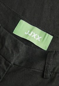 Zwarte stof met een gestructureerde afwerking, met een groene kledinglabel waarop "JJXX" in witte letters staat.