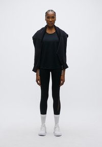 Μαύρο αθλητικό σύνολο με κοντομάνικη μπλούζα και κολάν. Το κολάν έχει διαφανή τμήματα. Το μοντέλο φοράει λευκά αθλητικά παπούτσια και κάλτσες.