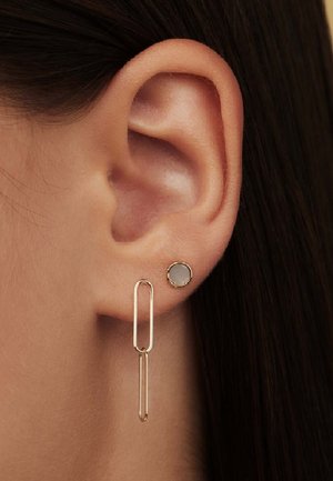 Goldene Ohrringe mit einer geometrischen Büroklammerform und einem kleineren runden Stecker, akzentuiert durch einen hellgrauen Stein in der runden Fassung.