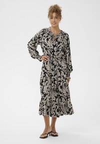 Rochie midi neagră cu un model paisley în crem, talie elastică, mâneci lungi și tiv volanat. Având un decolteu tip cheie și un design fluid.