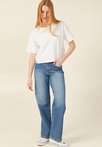 Witte katoenen t-shirt met kantdetails aan de zijkanten, gecombineerd met lichtblauwe rechte jeans en witte sneakers.