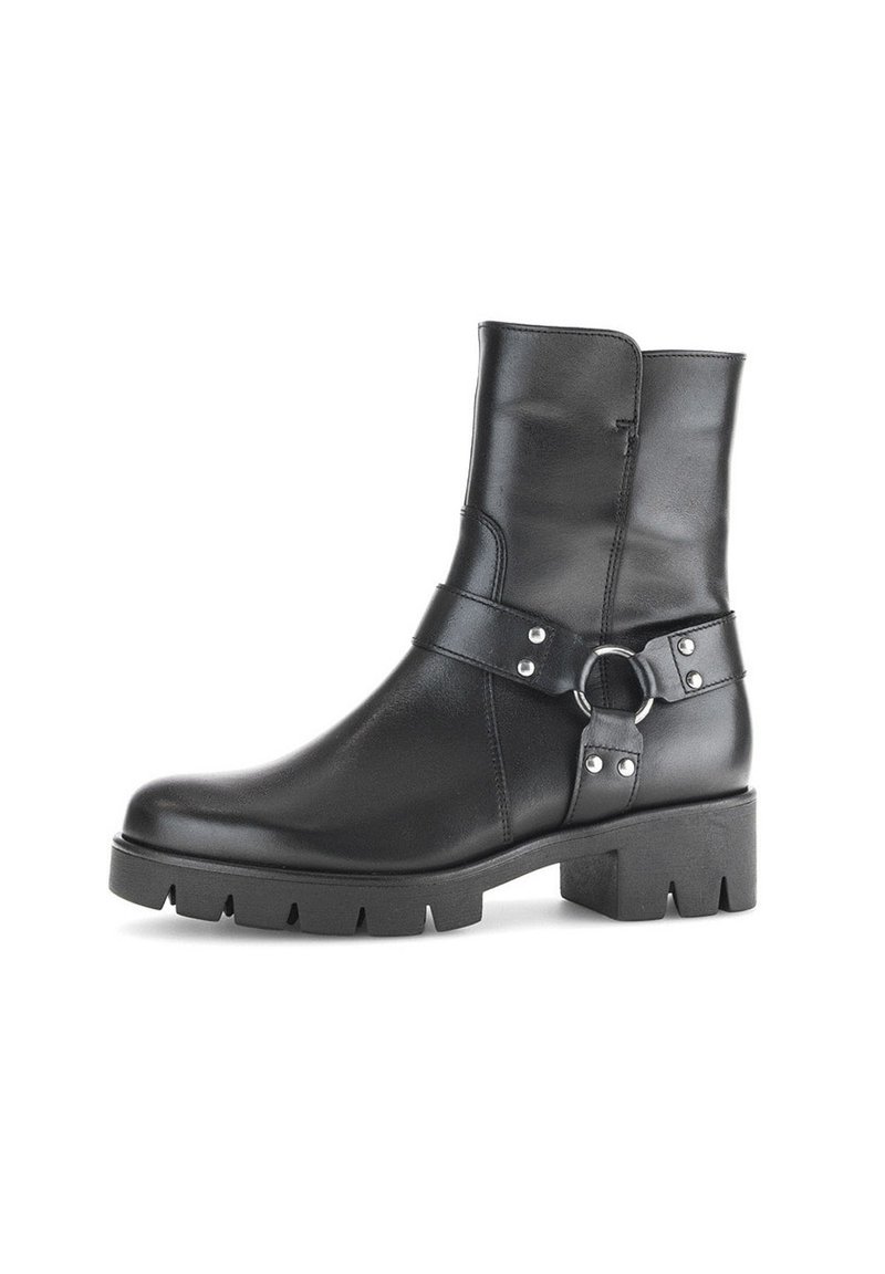 Stivale alla caviglia in pelle nera con suola spessa, tacco a blocco e cinturino decorativo con anello metallico e ribattini attorno alla caviglia.