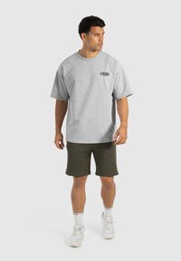 Camiseta de algodón gris de corte oversize con mangas cortas y cuello redondo, combinada con pantalones cortos verde oscuro y zapatillas blancas.