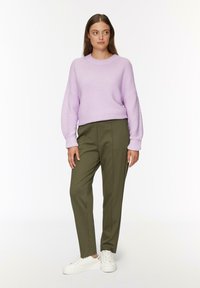 Lichtpaarse geribbelde trui met brede mouwen, gecombineerd met op maat gemaakte olijfgroene broeken en witte sneakers. Eenvoudige, hedendaagse outfit.
