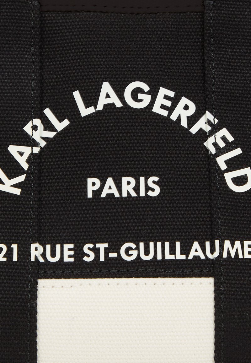 Toile noire avec texte blanc, présentant "KARL LAGERFELD," "PARIS," et "21 RUE ST-GUILLAUME." Le texte est en gras, moderne et centré.