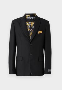 Blazer nero con due bottoni, reverse a scollo, e tasche laterali. Foderato con un tessuto a fantasia con dettagli dorati e bianchi. Etichetta sulla tasca.