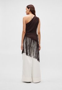 Bruin off-shoulder top met franjes, gecombineerd met witte broek met wijde pijpen. Gladde stoftextuur, asymmetrische zoom en minimalistisch ontwerp.