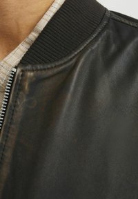 Giubbotto bomber in pelle nera con colletto a coste nera e zip argentata, con una finitura текстurizzata e cuciture visibili.