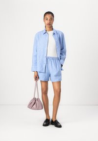 Chemise rayée bleu clair et short assorti en tissu doux ; associé à un sac à cordon rose et des mocassins noirs.