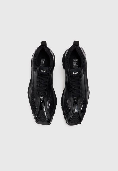 Schwarze Sportschuhe aus Mesh und synthetischen Akzenten, mit einer strukturierten Sohle, auffälligen Schnürsenkeln und einer kleinen Schlaufe an der Ferse.
