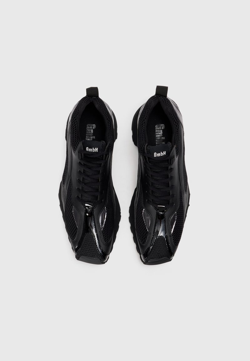 Zwarte atletische schoenen met gaas- en synthetische accenten, met een gestructureerde zool, opvallende veters en een kleine lus bij de hiel.