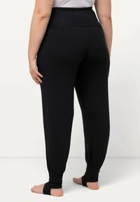 Pantalones negros de cintura alta con un ajuste tapered. Presentan una tela suave y elástica, con cortes en los tobillos. Textura lisa sin patrones visibles.