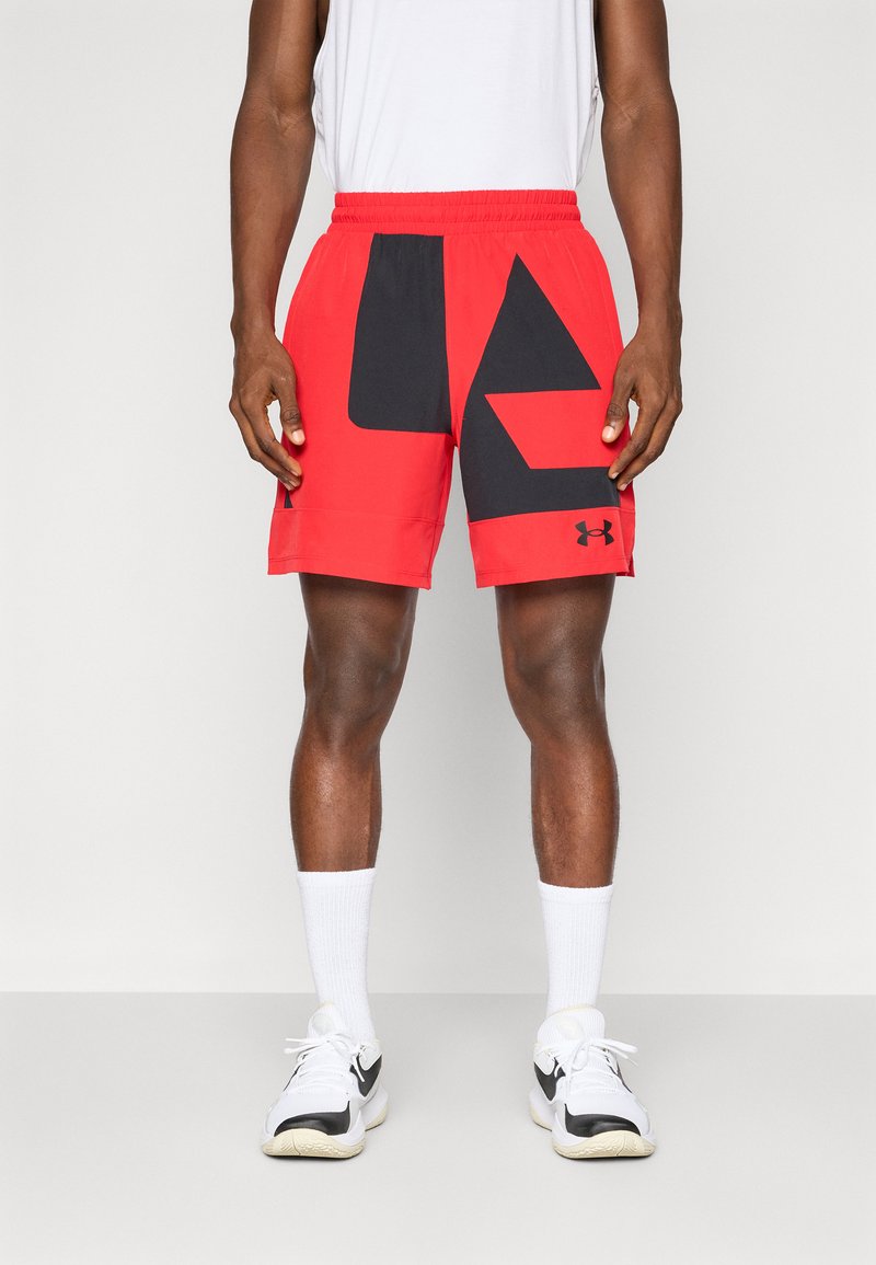 Rode shorts met een zwart geometrisch design op het linkerbeen en een elastische tailleband, gecombineerd met witte sokken en zwart-witte sport schoenen.