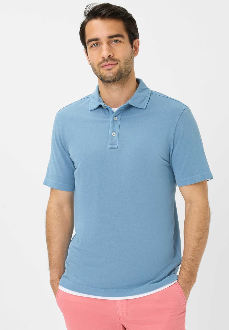 Lyseblå polo shirt i et blødt stof med krave, tre knapper og korte ærmer. Bæres med lyserøde shorts.