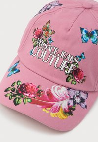 Roza bejzbol kapa s cvjetnim i motivima leptira, s logom "Versace Jeans Couture". Izrađena od tkanine, strukturiranog dizajna s zakrivljenim vizirima.