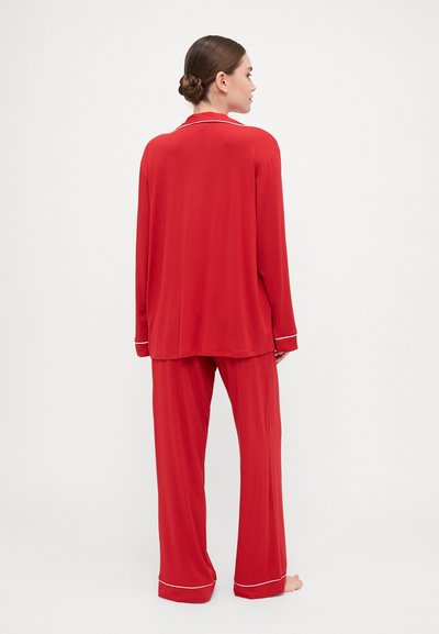 Red pajama set made of soft fabric. Features a long-sleeved top with a collar and contrasting white piping, paired with loose-fitting pants.