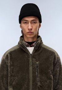 Fleece-takki tummanoliivinvihreänä, jossa on vetoketju edessä, korkea kaulus ja rintatasku. Sisältää teksturoitua kangasta ja erottuvat olkapanelit.