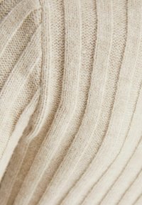Gräddfärgad stickad tröja med ribbat mönster och vertikala ränder. Tyget verkar mjukt och varmt, perfekt för kallt väder.