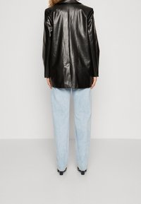 Blazer de cuero negro con textura lisa, con una sola abertura en la parte trasera, combinado con vaqueros de tiro alto azul claro y tacones oscuros.