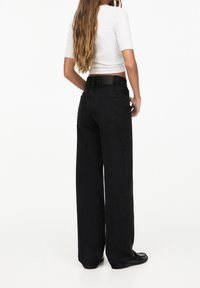 Jeans de pierna ancha negros, hechos de mezclilla, que cuentan con un diseño clásico de 5 bolsillos, detalles de costura sutiles y una cinturilla negra con marca en la parte posterior.