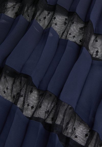 Laivastonsininen laskostettu kangas, jossa on kerroksia läpikuultavaa verkkoa, jossa on pilkkukuosi. Kangas vaikuttaa pehmeältä ja siinä on havaittavissa hieno kiilto.