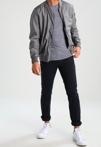 Grå bomberjacka i strukturerat material med ribbade ärmslut, lager på en melerad grå T-shirt. Kombinerad med mörka slim-fit byxor och vita sneakers.