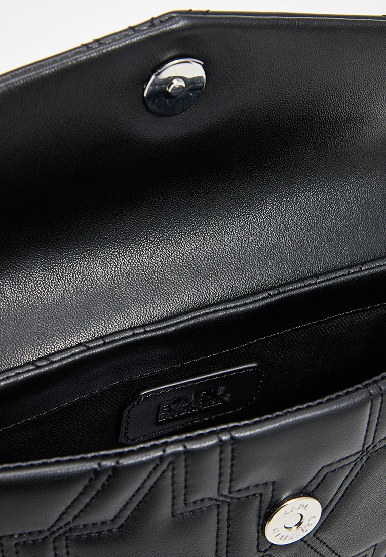 Interno di una borsa a mano in pelle nera con texture trapuntata, chiusura a scatto in argento e etichetta con brand. Finitura liscia, design minimalista.