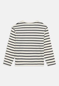 Dolga majica z dolgimi rokavi iz krem bombaža s črnimi vodoravnimi črtami. Okrogel izrez in detajli šivov ob robu in rokavih.