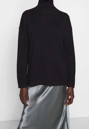 Pull col roulé noir à manches longues porté avec une jupe en satin argenté brillant, présenté du cou jusqu'à mi-cuisse sur un fond uni.