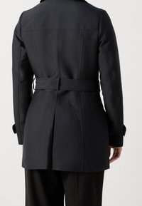 Manteau noir croisé avec une taille cintrée, détail de ceinture et texture lisse. Comprend des coutures verticales et des poignets ajustables.