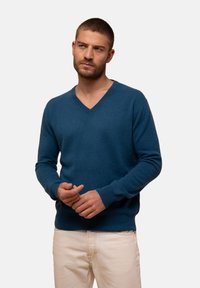 Svetr s V výstřihem v tmavě modré barvě, vyrobený z měkkého pleteného materiálu s žebrovanými manžetami a lemem. Lehce a přiléhavý design.