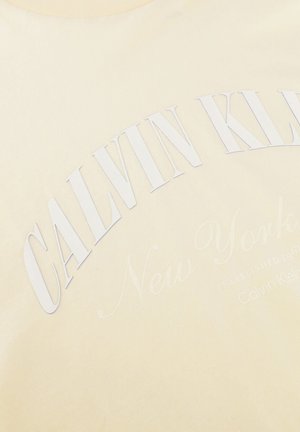 Tissu beige avec texte blanc en relief « CALVIN KLEIN » en grandes lettres, et texte cursif pâle « New York » en dessous.