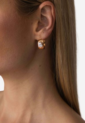 Goldener Creolenohrring mit klarem Edelsteinakzent. Der Ohrring verfügt über eine glatte, polierte Oberfläche und ein rundes, massives Design.