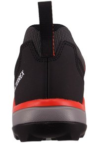 Black athletic shoe with a mesh upper, red sole, and pull tab. Features textured materials and a low-profile design for comfort.